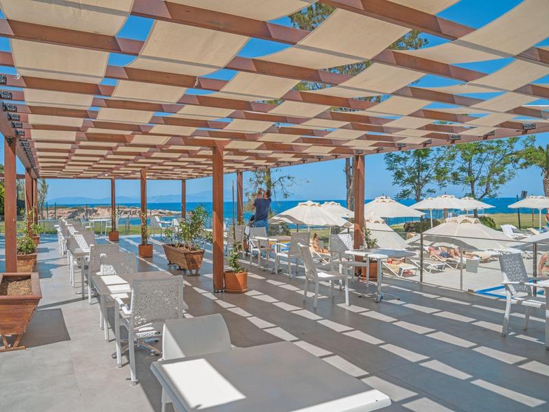 Überdachte Terrasse mit Sitzgelegenheiten und Blick auf Strand und Meer unter blauem Himmel.