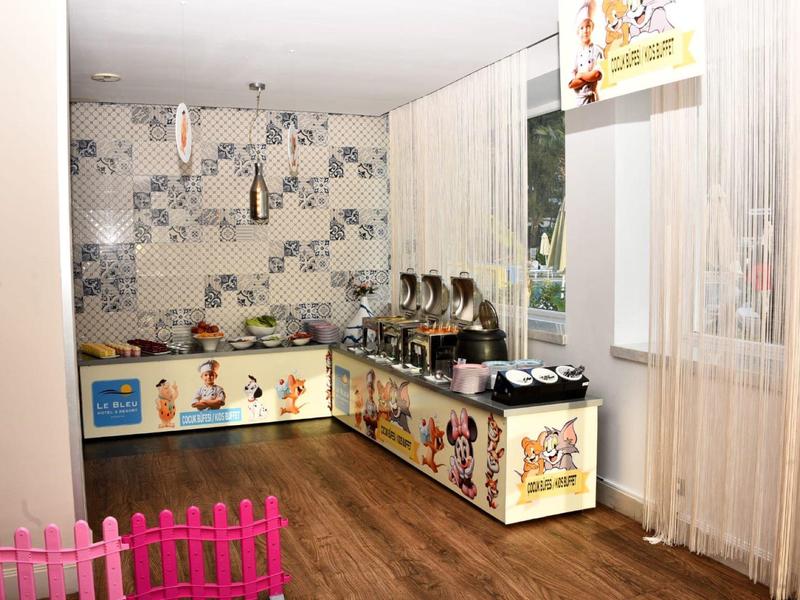 Kinderküche mit bunten Schränken, Spielzeuggeschirr und Hintergrundtapete in warmen Farben.