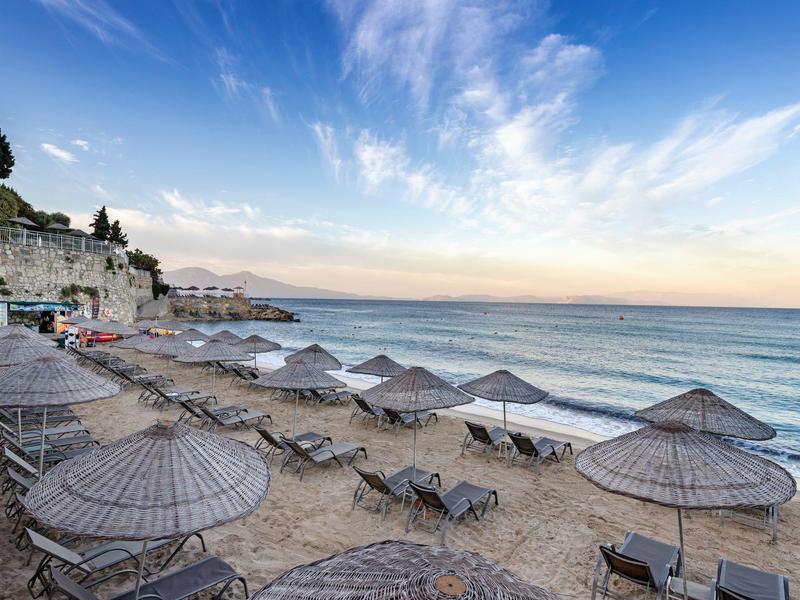 Beach with rows of empty sun loungers and parasols under a blue sky with scattered clouds.