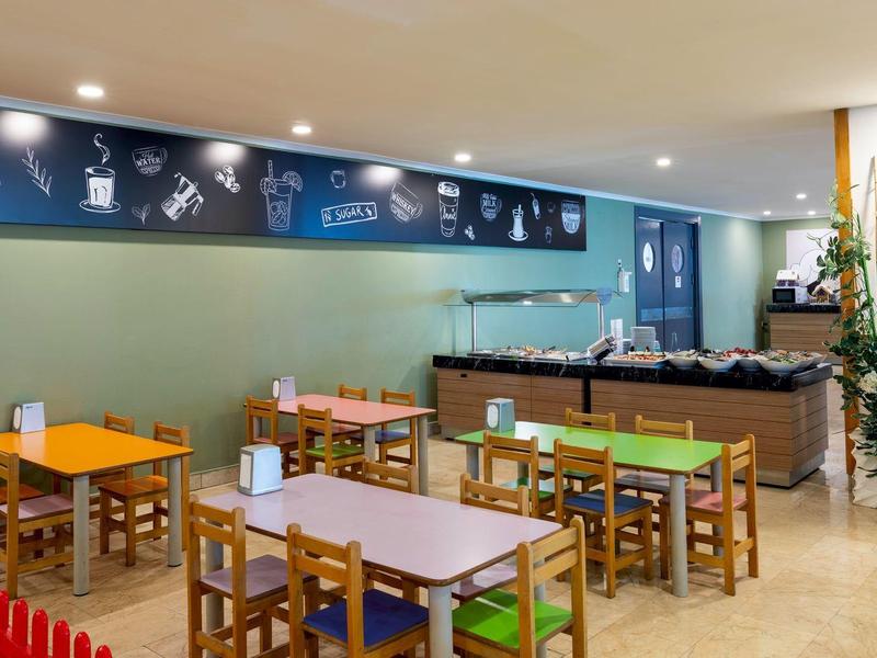 Children's play area with small tables and chairs near a hotel lobby or buffet area.