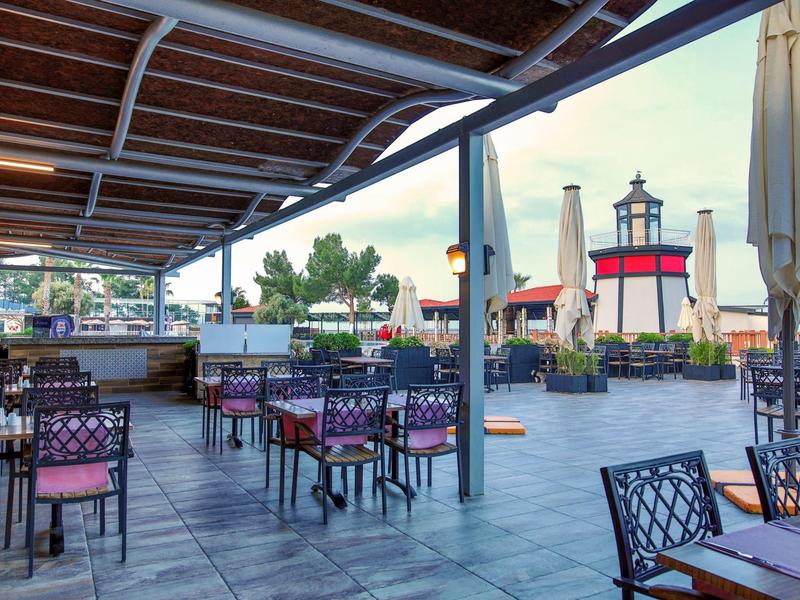 Outdoor restaurant seating with tables and chairs under a covered patio near a lighthouse.