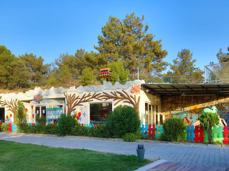 Colorful hotel exterior with artistic wall painting and lush greenery under a clear blue sky.