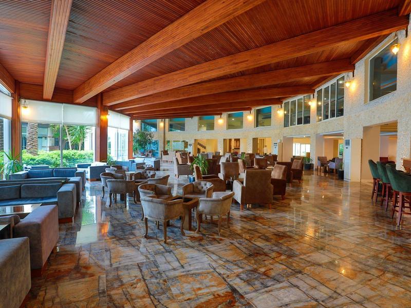 Spacious hotel lobby with wooden ceiling, marble floors, seating areas, and large windows.