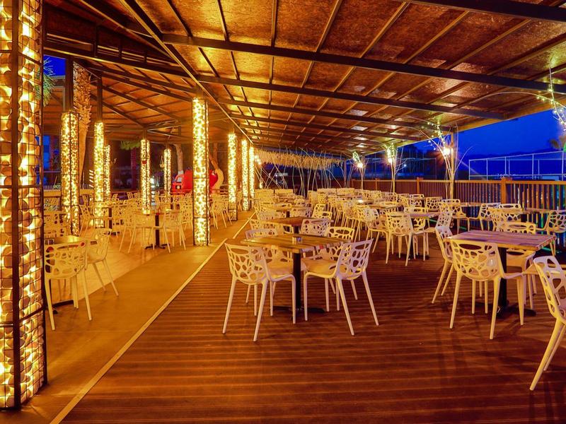 Spacious outdoor terrace with wooden floor, elegant lighting, and multiple empty tables and chairs.