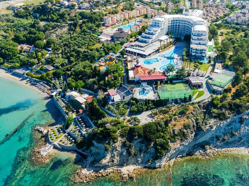 Aerial view of a coastal resort with buildings, pools, tennis courts, and surrounding greenery.