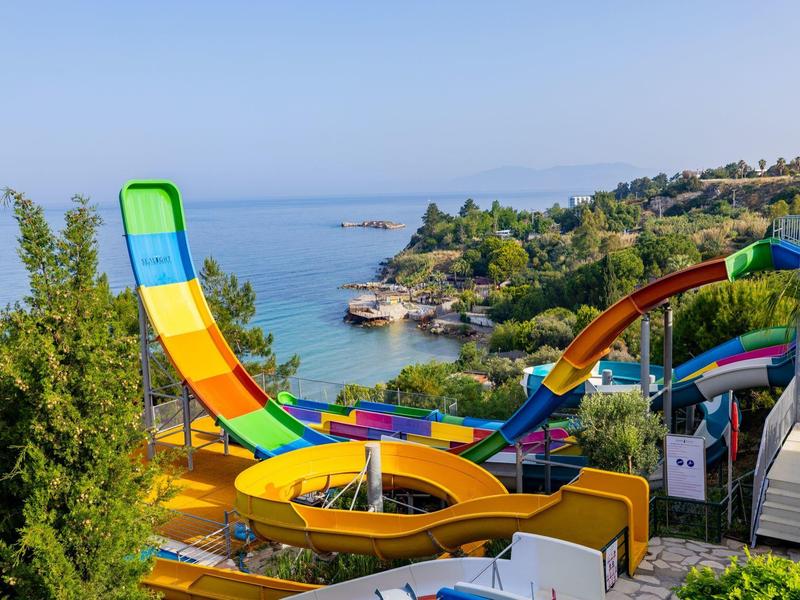 Colorful water slides winding down towards a coastal area with blue sea and green trees.
