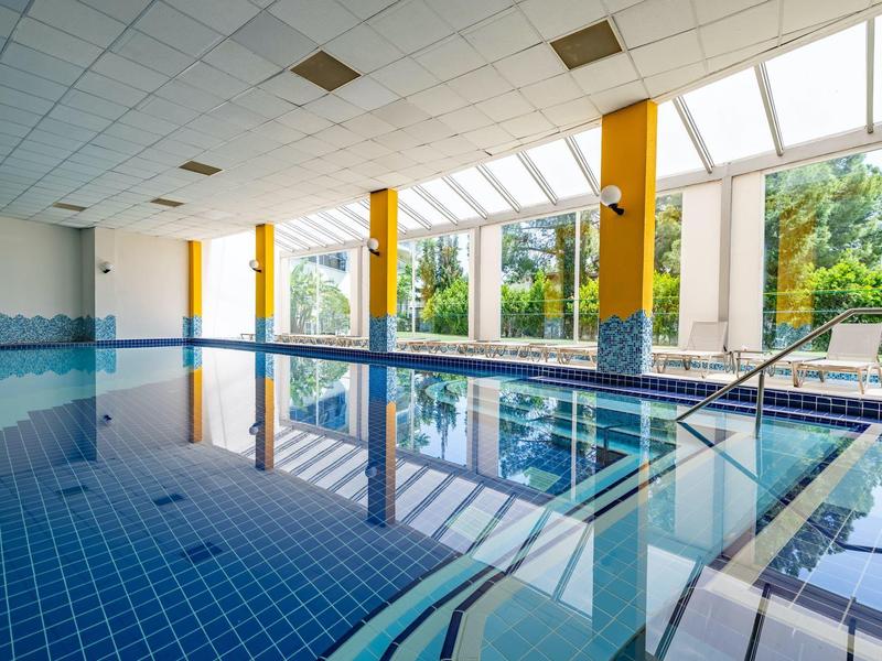 Indoor swimming pool with clear water, large windows, and yellow pillars in a bright room.