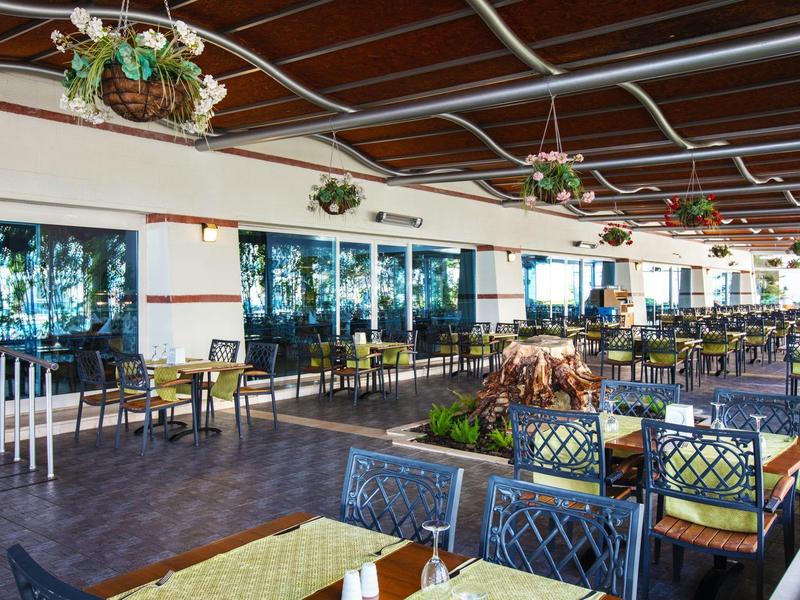 Spacious outdoor terrace with tables and chairs under a wooden roof, decorated with hanging flower baskets.