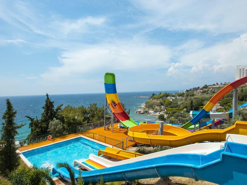 Water park with colorful slides near the blue sea and green coastal landscape.