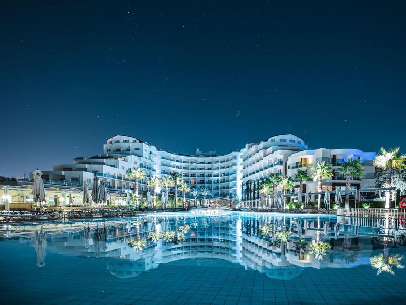 Luxurious hotel at night with pool reflecting the building and clear starry sky.
