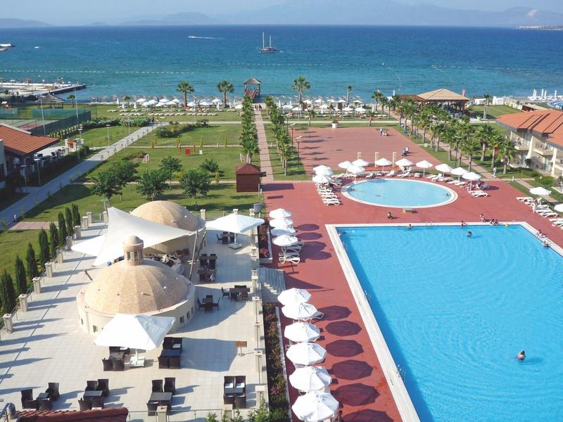 Große Hotelanlage mit mehreren Pools, Sonnenschirmen, grünen Rasenflächen und Blick aufs blaue Meer.