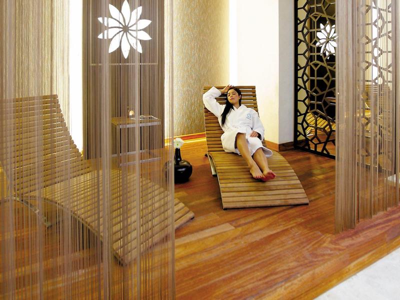 Frau entspannt auf Holzliege in modernem, warm beleuchtetem Spa mit dekorativen Trennwänden.