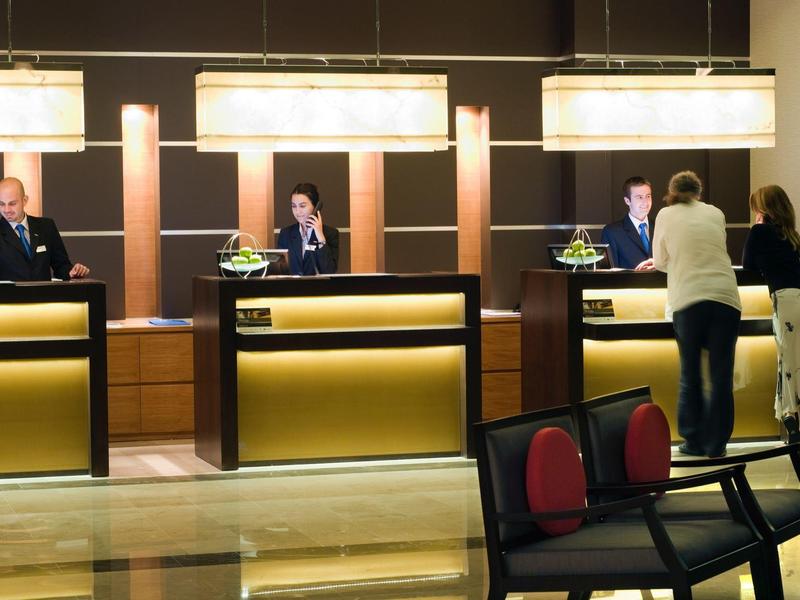 Hotelrezeption mit drei beleuchteten Tresen, Gästen und Empfangspersonal in moderner, stilvoller Umgebung.