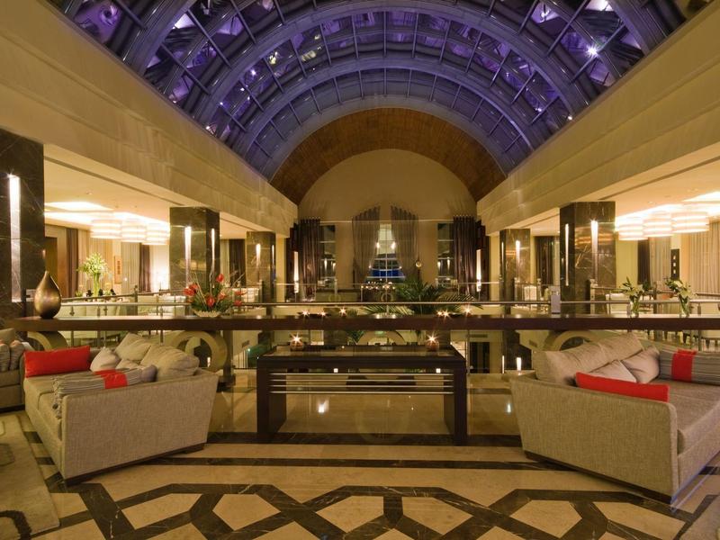 Großer Hotel-Lobby mit hohen Decken, Sofas, Lampen und elegantem Bodenmuster bei Abendlicht.