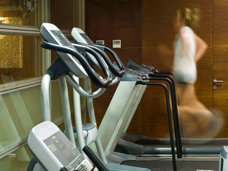 Mehrere Laufbänder in einem Fitnessstudio, eine Person joggt schnell auf einem davon.