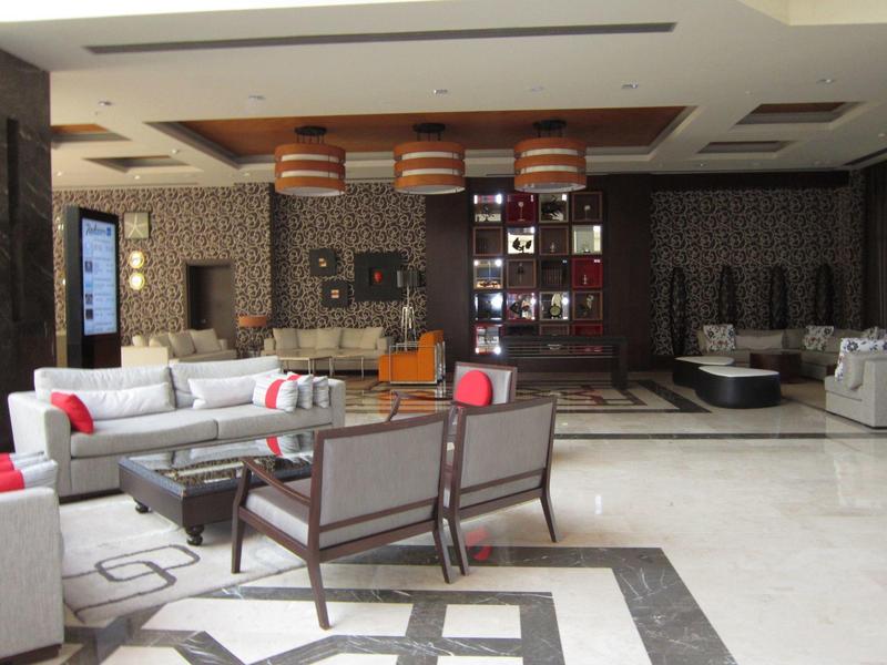 Großer, moderner Wohnraum mit grauen Sofas, dunkelroten Kissen und hölzernen Leuchten unter Decke.