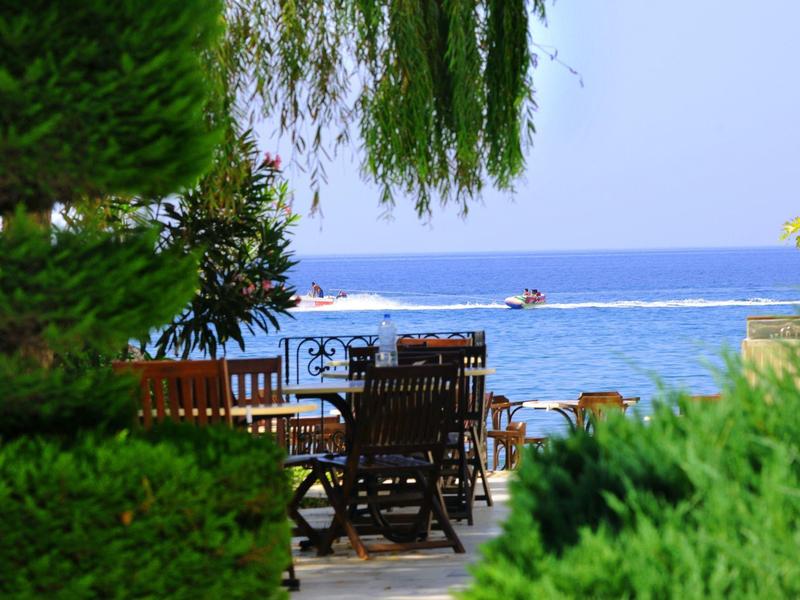 View of a terrace with wooden chairs and tables, with the sea and clear sky in the background.