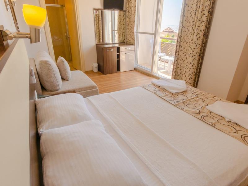 Světý hotelový pokoj s manželskou postelí, pohovkou, televizí a balkonem s výhledem na moře.