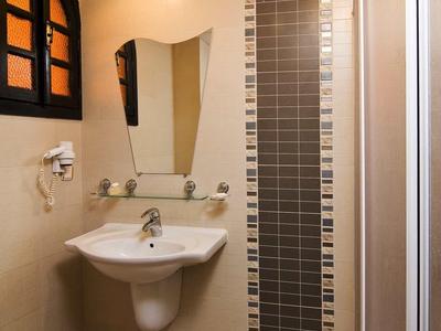 Badezimmer mit Waschbecken, spiegel, Duschkabine und gelben Wänden mit kleiner Fensteröffnung.