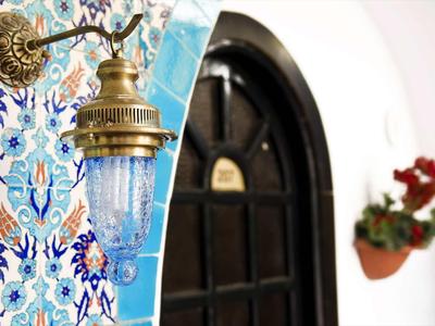 Wandlampe mit blauem Glas und Messing, neben bunter Fliesenwand und schwarzer Holztür mit Blumen.