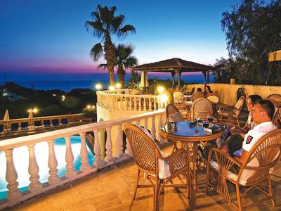 Terrassenbereich mit runden Tischen und Stühlen, Pool, Palmen und Abendhimmel mit Dämmerung.