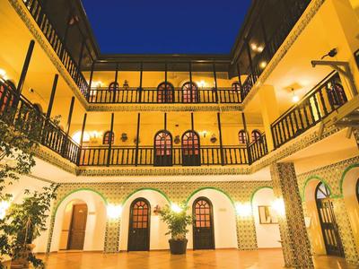 Innenhof eines Gebäudes mit drei Etagen, gelben Wänden, Balkonen und abendlicher Beleuchtung.