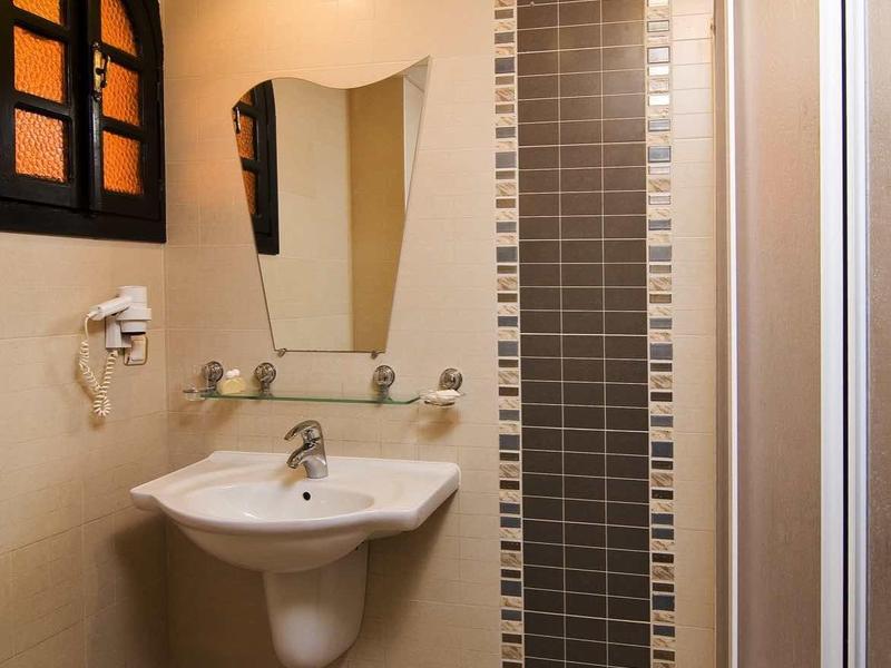 Badezimmer mit Waschbecken, spiegel, Duschkabine und gelben Wänden mit kleiner Fensteröffnung.