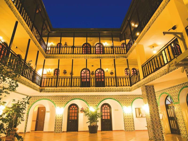 Innenhof eines Gebäudes mit drei Etagen, gelben Wänden, Balkonen und abendlicher Beleuchtung.