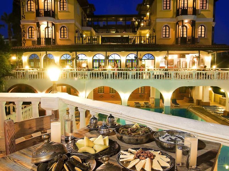 Beleuchtetes mehrstöckiges Gebäude mit Balkon und Pool, im Vordergrund gedeckter Tisch mit Speisen.