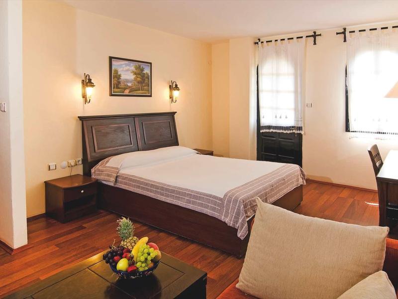 Gemütliches Schlafzimmer mit Holzboden, Doppelbett, Fenster und gemütlichem Sitzbereich.