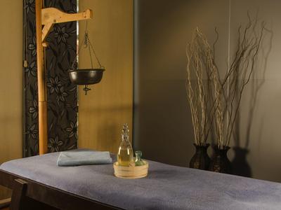 Une salle de massage tranquille avec une table de massage, un bol sur un support en bois et des branches décoratives dans le coin.