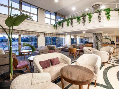 Světla hotelová hala s pohodlnými křesly, dřevěnými stolky a velkými okny s výhledem ven.