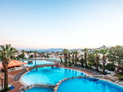 Vue de deux piscines rondes avec des palmiers et vue sur la mer sous un ciel clair.