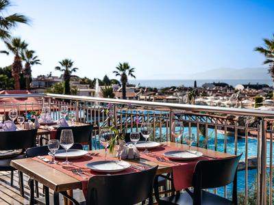 Terasa restaurace s prostřenými stoly s výhledem na bazén a palmy pod ní.