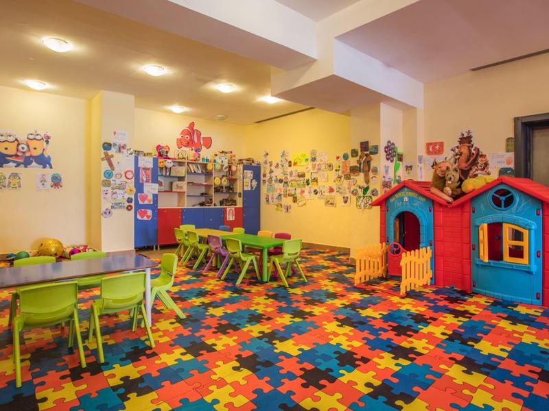 Barevná herna s domečkem, stoly a výrazným kobercem v hotelu pro děti.