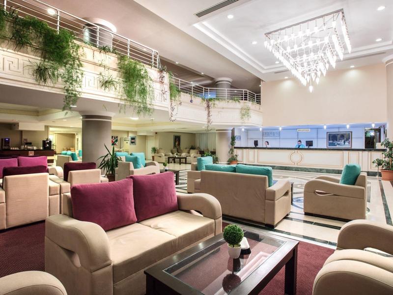 Moderní hotelová hala s pohodlnými pohovkami, skleněnou zdí a zavěšenými rostlinami