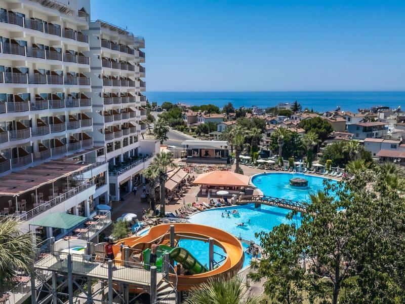 Hotel s několika bazény obklopenými palmami a výhledem na moře za jasné oblohy.