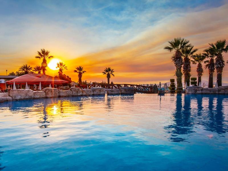 Bazén s palmami a západem slunce v tropickém hotelovém resortu