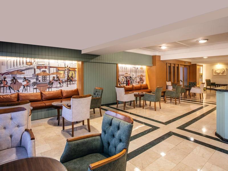 Moderní hotelová restaurace s stoly, židlemi a dekorativními obrazy na stěnách.