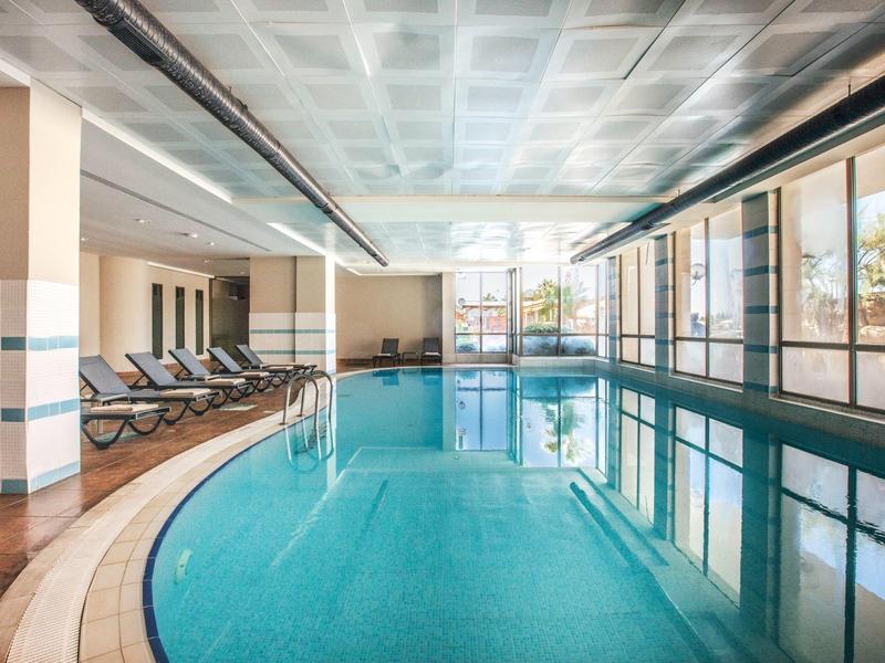 Vnitřní hotelová oblast s velkým obdélníkovým bazénem a lehátky podél strany.