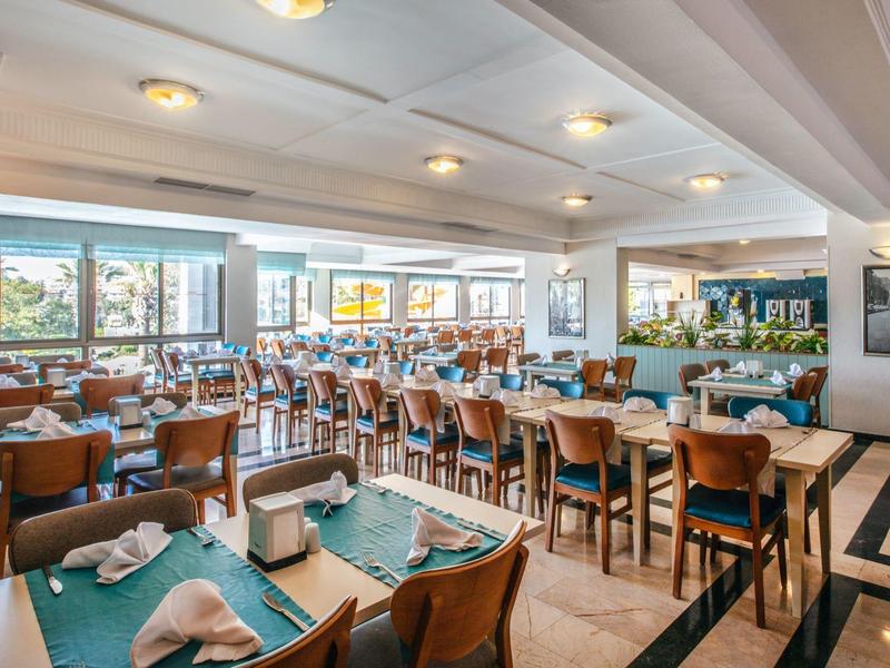 Velká světlá restaurace s mnoha stoly a židlemi, moderní interiér a velká okna.