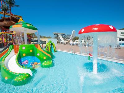 Waterpark met kleurrijke glijbanen en paddestoel waterattracties in het zwembad onder een blauwe lucht.