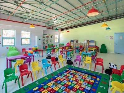 Kleurrijke kinderkamer met kleine stoelen, speelgoed en een fel tapijt in een lichte ruimte.