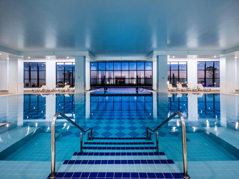 Groot modern binnenzwembad met trap en panoramische ramen met uitzicht op de zonsondergang.