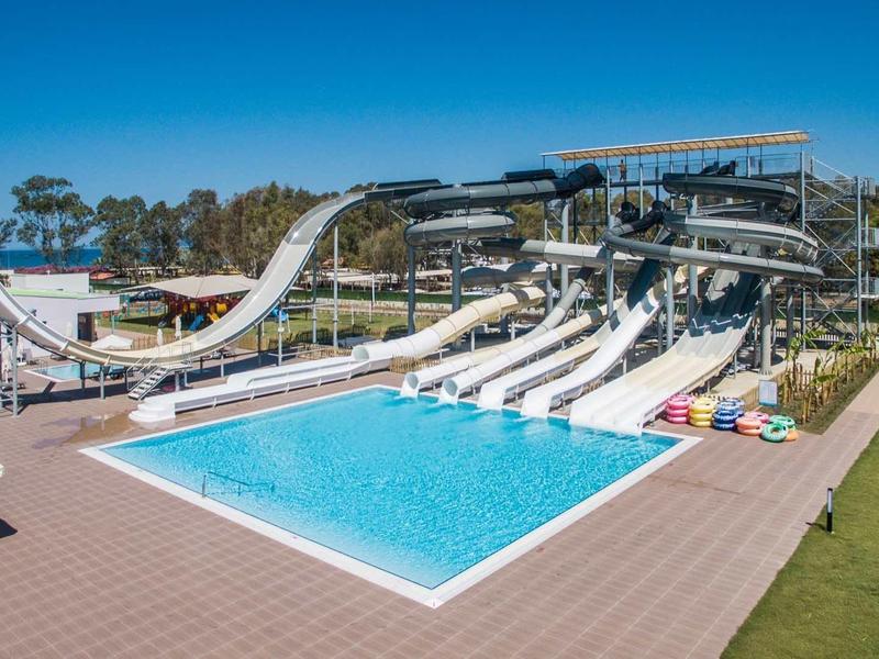 Groot waterparkzwembad met meerdere witte glijbanen en parasols onder een blauwe hemel.