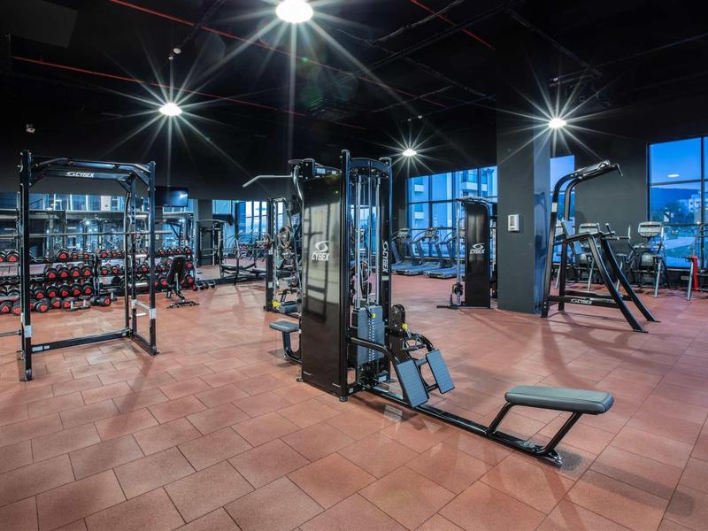 Grote fitnessruimte met trainingsapparatuur en gewichten, verlicht tijdens schemering.