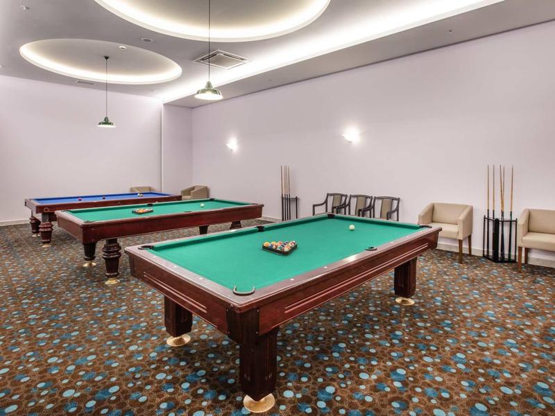 Interieur met twee pooltafels, gestoffeerde stoelen en plafondlampen in een recreatieruimte.