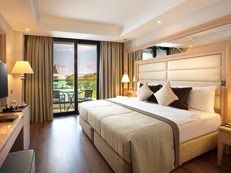 Modern hotelkamer met groot bed, balkon en zonsondergang over golfbaan.