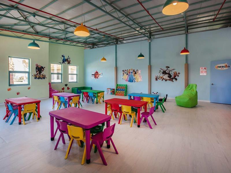 Kleurrijke speelkamer voor kinderen met kleine tafels, stoelen en levendige decoraties.