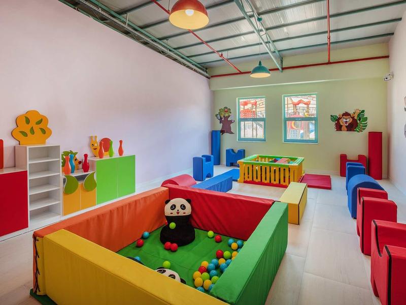 Kleurrijke kinderspeelruimte met ballenbak, zithoeken en wanddecoraties in een lichte kamer.